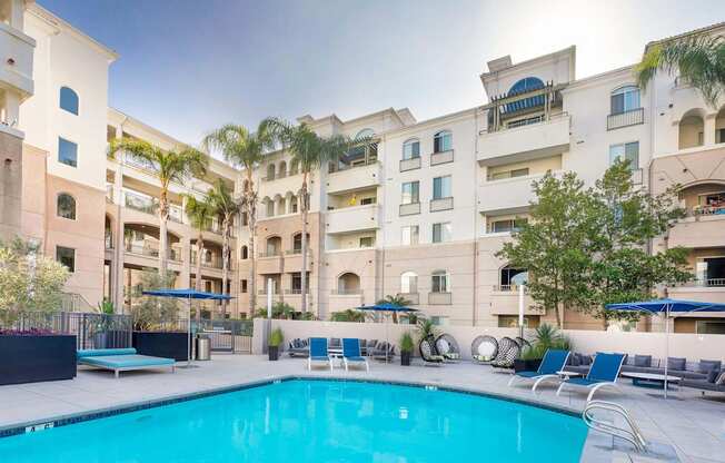 A swimming pool in front of a building with a blue umbrella. at La Jolla Crossroads Apartments, San Diego, 92122