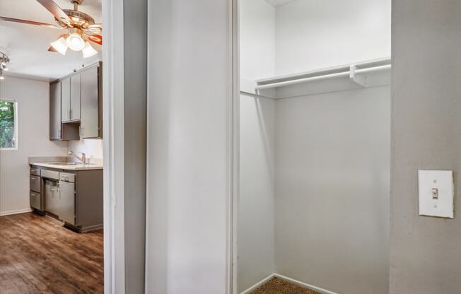 an empty room with an open door to a kitchen and a ceiling fan