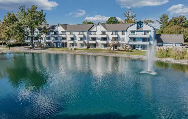 a fountain in the middle of a lake with an apartment building in the background