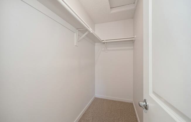 A large extended bedroom closet with a white door and white walls