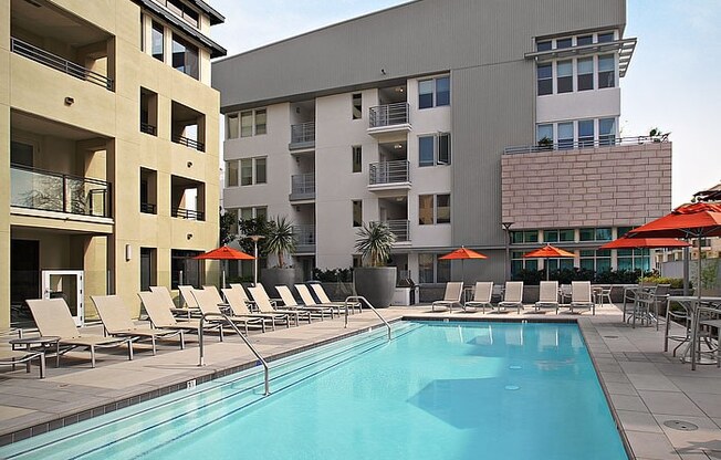 a swimming pool with chaise lounge chairs and umbrellas in front of a building