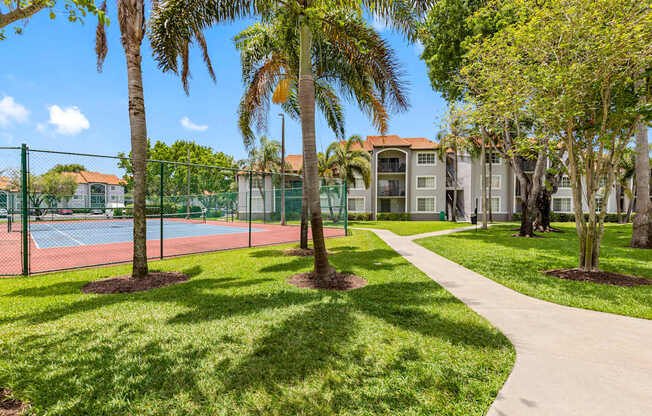 A tennis court is surrounded by a green fence and trees.