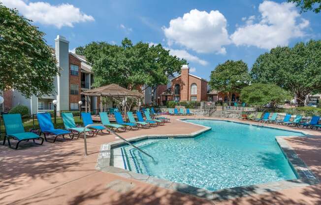 a resort style swimming pool with blue chairs and a building in the background