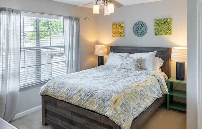 A bedroom with a bed, a ceiling fan, and a window with curtains.
