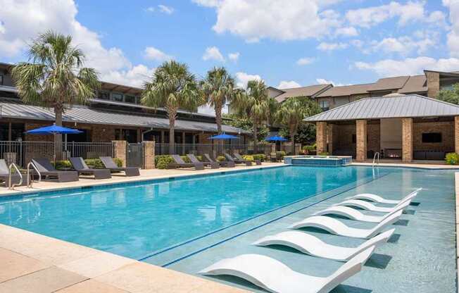 A large swimming pool with lounge chairs and umbrellas in front of a building.