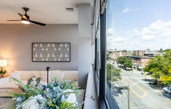 A living room with a couch, a fan, and a window overlooking a street.