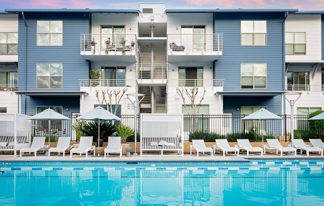 A large blue and white apartment building with a pool in front.
