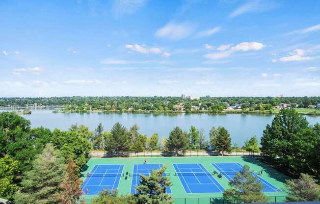 A tennis court surrounded by trees and a body of water.