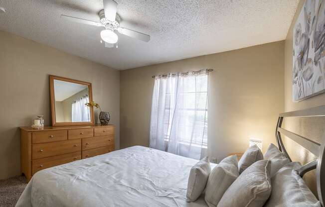 A bedroom with a bed, dresser, mirror, and a ceiling fan.