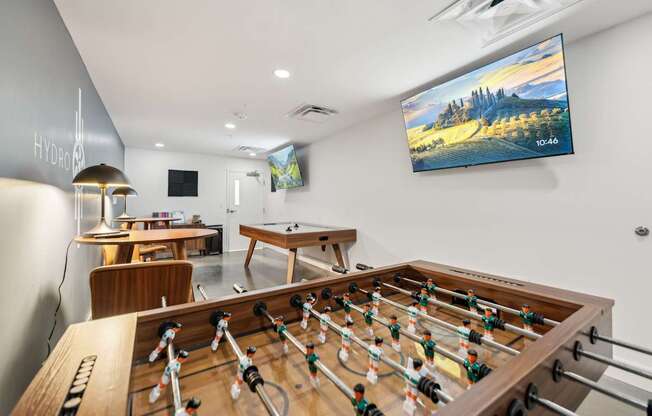 A foosball table is in the middle of a room with a pool table and a ping pong table.