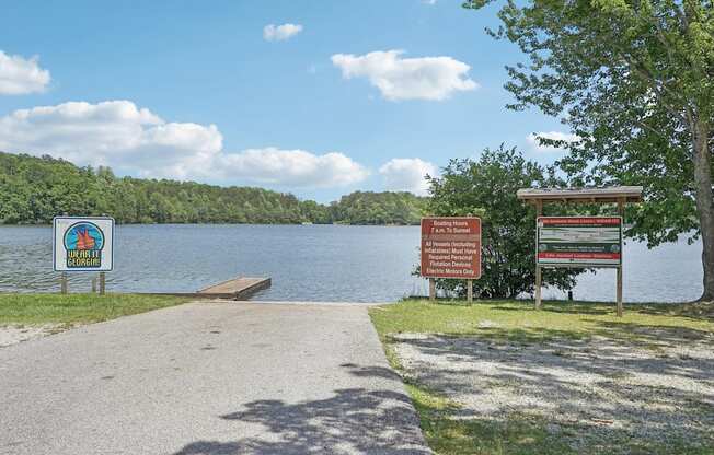 A signboard with a logo and text is placed on a grassy area near a lake.