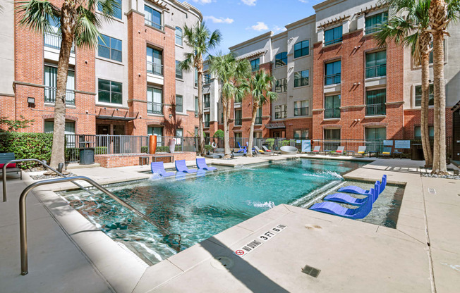 a swimming pool with blue lounge chairs in front of an apartment building