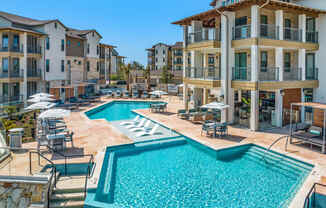 a swimming pool with chairs and umbrellas in front of an apartment building
