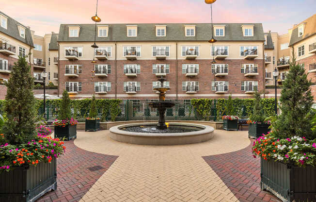 A courtyard with a fountain surrounded by flower pots and buildings in the background.