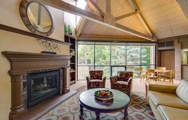 Community room with chairs facing fireplace, high ceilings with wooden archways, and large windows