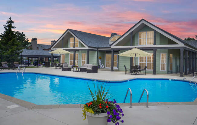 A fenced in swimming pool next to outdoor chairs and tables with umbrellas.