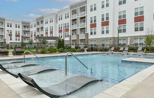A large swimming pool with lounge chairs in front of apartment buildings.