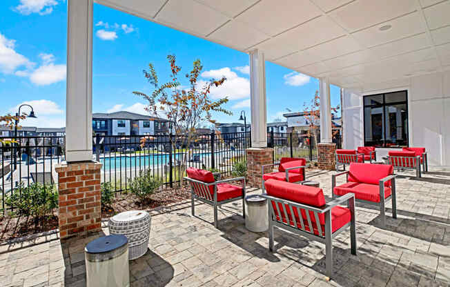 a covered patio with red chairs and tables and a pool