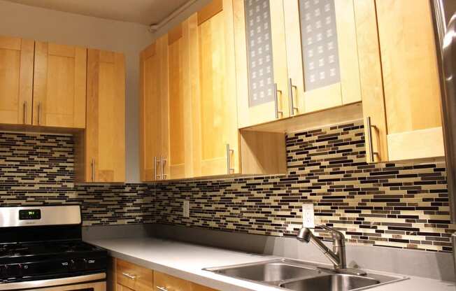 A kitchen in Brookmore apartments in Pasadena ca with modern, honey wood cabinets, multicolored tile backsplash, six burner gas stove, and dual sink