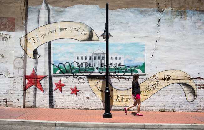 A woman walks past a mural of a white house with a banner that reads "If you find here you're lost".