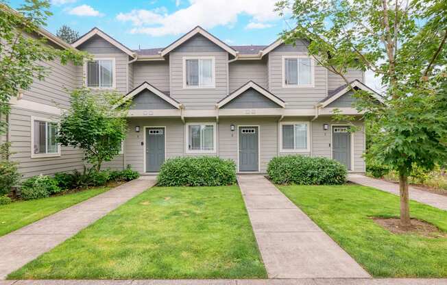 the front of a grey house with a sidewalk and grass