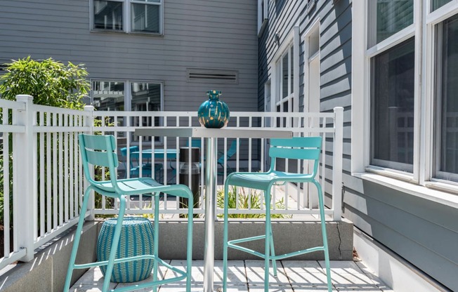 a small patio with blue chairs and a small table with a teal vase on it