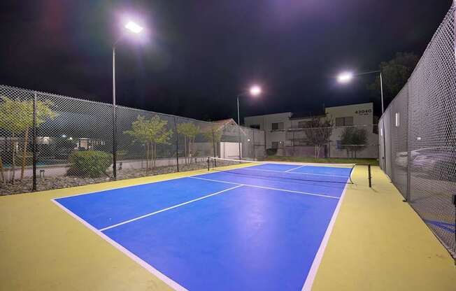 A tennis court is lit up at night with bright lights.
