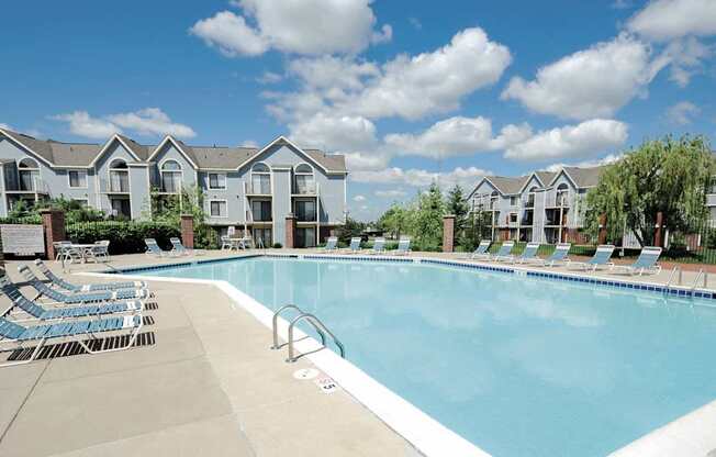 A large swimming pool with lounge chairs and apartment buildings in the background.