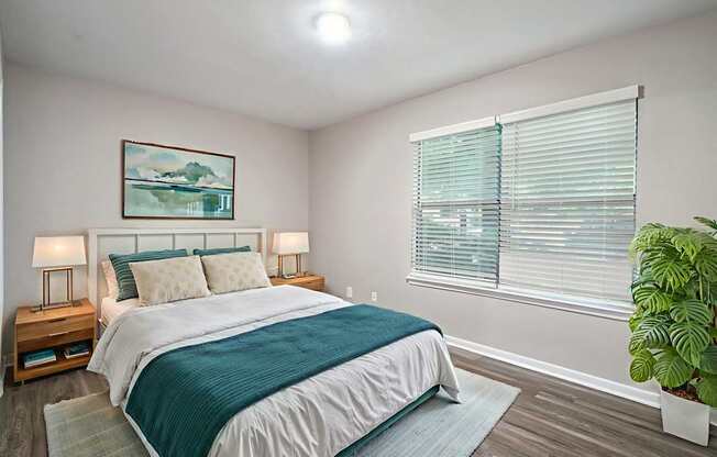 A bedroom with a bed, two lamps, and a potted plant.