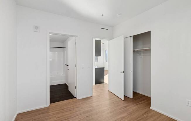 A room with white walls and wooden floors with open doors.