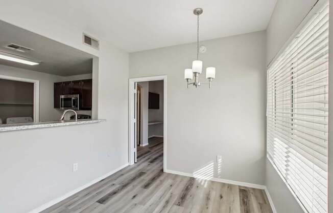 A room with a chandelier and a kitchen area in the background.