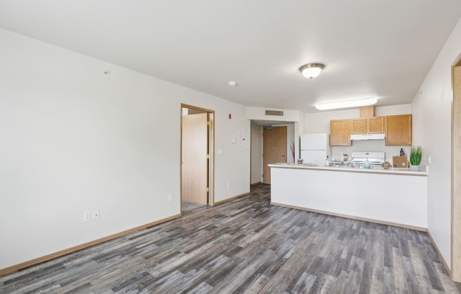 the living room and kitchen of an apartment with white walls and wood floors