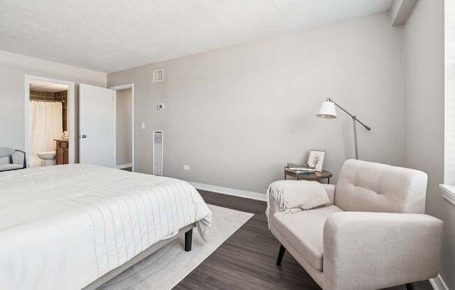 A bedroom with a bed, chair, and lamp.