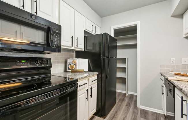 A black stove and refrigerator in a kitchen with white cabinets.