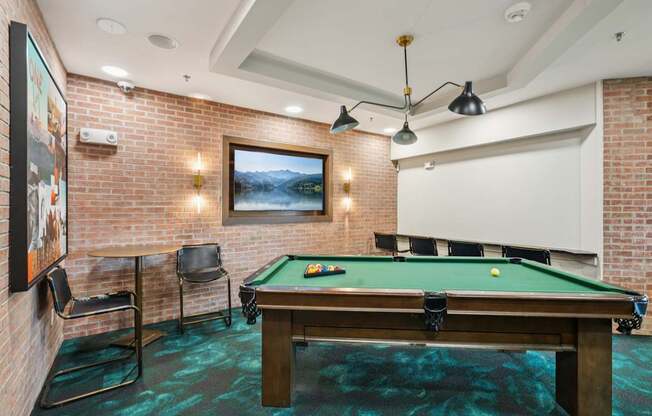 A pool table in a room with a brick wall and a painting hanging on it.