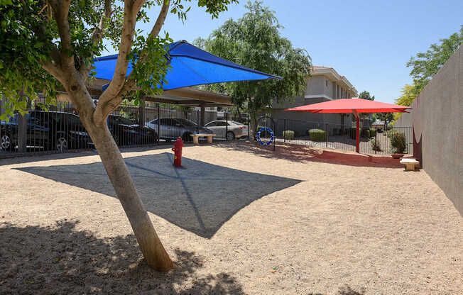 A tree in a yard with a blue umbrella and a red fire hydrant.