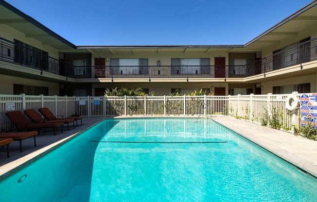 A swimming pool in front of a building with lounge chairs on the side.