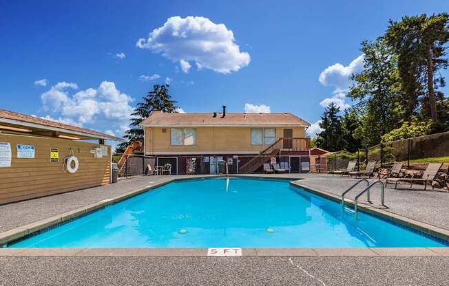 A large swimming pool in front of a building with a blue sky and clouds in the background.