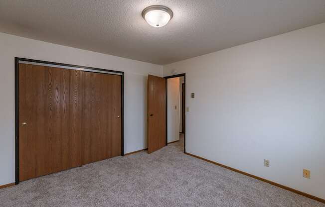 a room with a carpeted floor and a door to a closet. Fargo, ND West Oak Apartments.