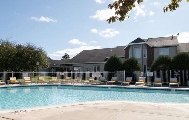 A pool surrounded by chairs and a building in the background.