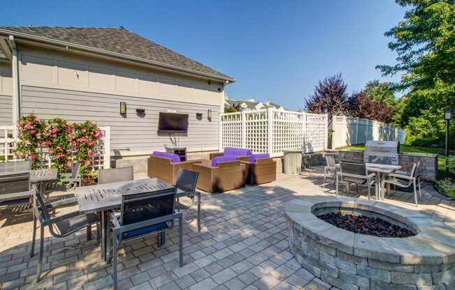 Fire pit with four person tables and grilling station with gas grill. Mounted outdoor TV with additional soft seating positioned in front.