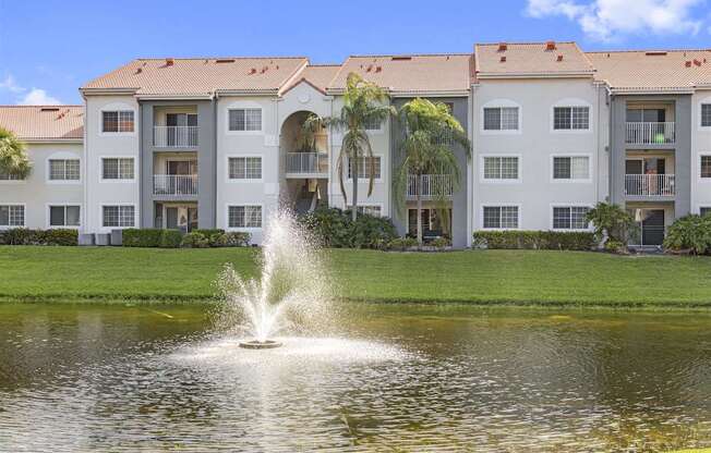 a fountain in the middle of a pond in front of some buildings