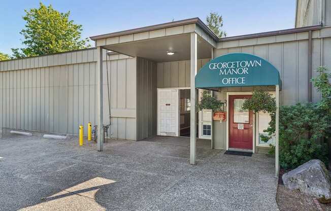 The Georgetown Manor Office is a small building with a red door and a green awning.