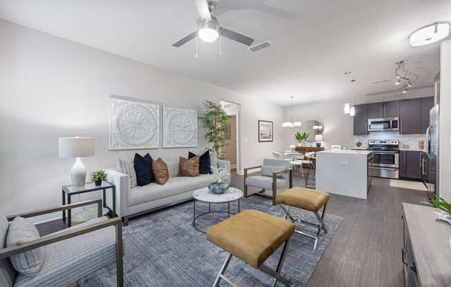 a living room with couches and chairs and a kitchen with a ceiling fan