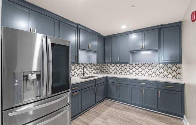 A kitchen with dark blue cabinets and a stainless steel refrigerator.