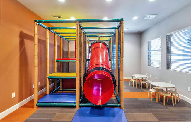 a large red slide in the middle of a room with a table and chairs in the background