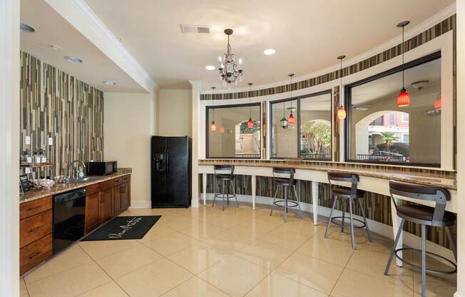 A kitchen with a black fridge and a bar area with stools.