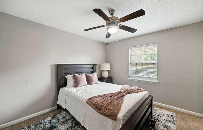 A bedroom with a bed, pillows, a blanket, a ceiling fan, and a rug.