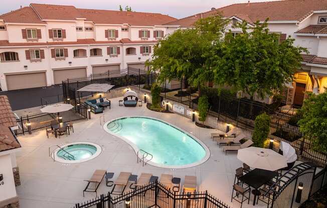 A large outdoor swimming pool surrounded by a black fence and patio furniture.