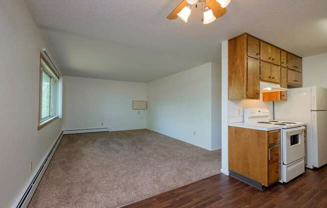 an empty living room with a kitchen with a stove and refrigerator. Fargo, ND Country Club Apartments.